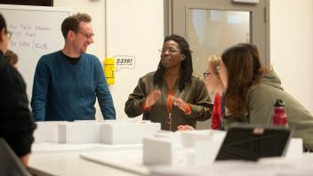 Left to right: Professor Tim McNeil, Department of Design, listens as Ama Bonsu talks about their layout as Millie Lozano and Zhou Zhou listen during the design exhibition class. 