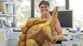 Evolutionary Geneticist Graham Coop smiling while holding blow-up dinosaur