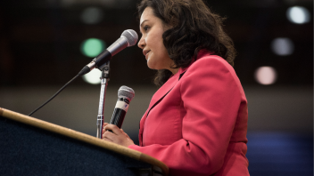 Professor Aldana speaking at a podium. The image is of her left profile as she is wearing a pink suit jacket and speaking into a microphone. 