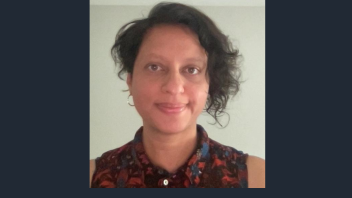 Head-and-shoulders portrait of a person with short curly hair, patterned top, neutral smile.