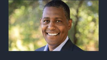 A headshot of Dean Ermias Kebreab. He is slightly turned to his left, smiling. Greenery is faded out in the background. 