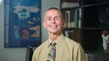 A headshot of Dr. Garen Wintemute smiling, wearing a green button up shirt and tie. 