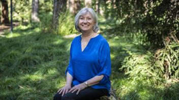 Patsy Owens sitting outside with a field of trees and greenery behind her. She is smiling with her hands on her knees. 
