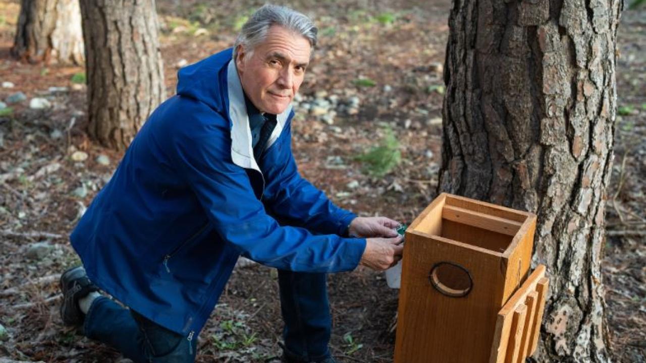 Prof. John Eadie kneeling next to a bee hive. 