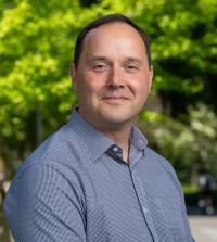 A headshot of Professor Neil Hunter in a button up shirt. There is greenery behind him.