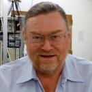 A middle-aged man with glasses and a beard smiles at the camera in an indoor setting.