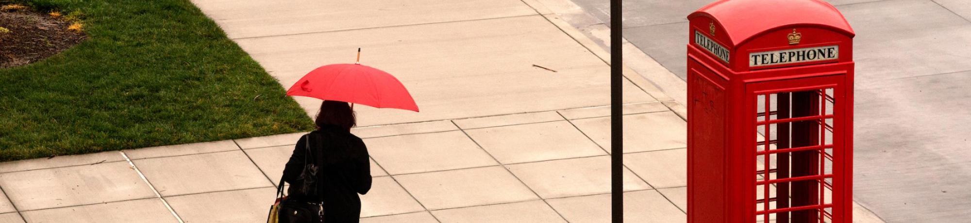 Woman with red umbrella walking past red phone booth