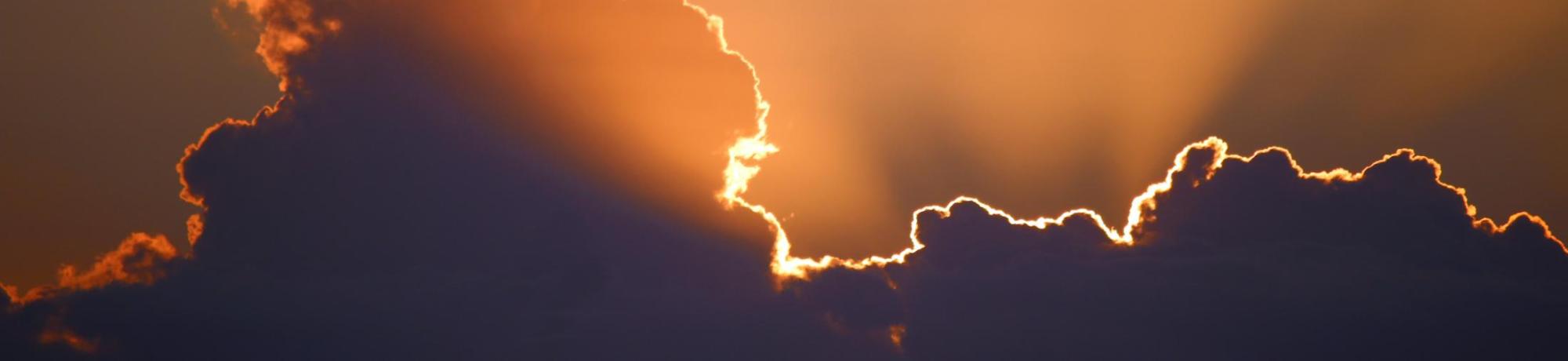 Serene sunrays beaming through a looming cloud. Photo by Marcus Dall Col on Unsplash