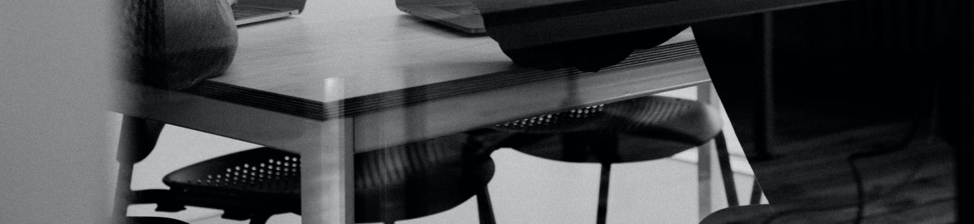 Photo by https://unsplash.com/@charlesdeluvio. A photo of an illusion. Two men are sitting next to one another at a table and have laptops in front of them. The man on the right has his left hand lifted, as though pointing at something on his screen. Although it's only the back of his head that you can see, he looks a bit frustrated.