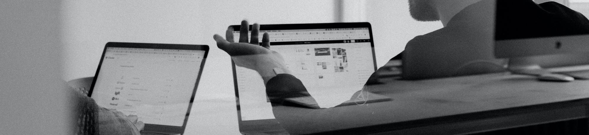 black and white photo of someone pointing at a laptop screen 